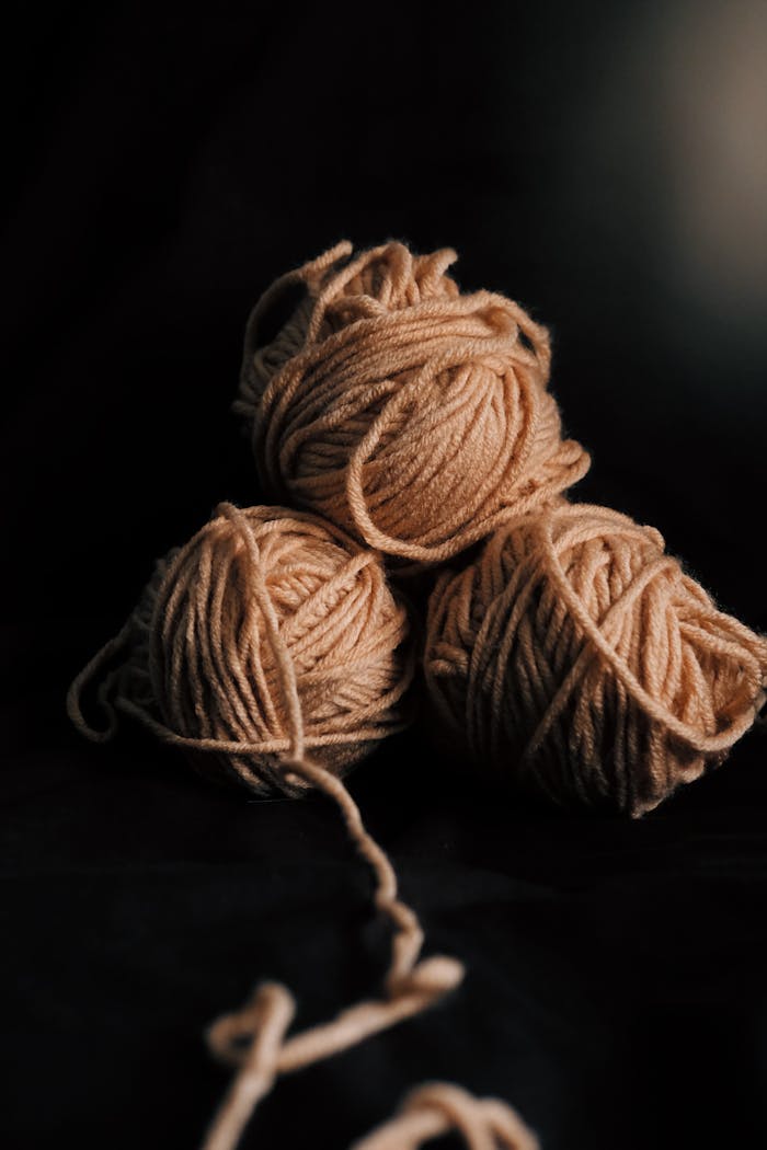 Three tan yarn balls with a black background, creating a cozy craft vibe.